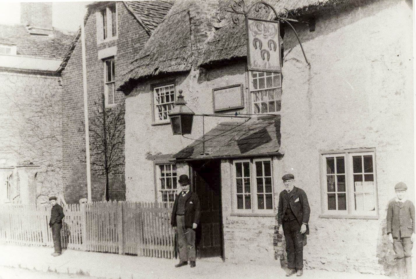 Three men standing outside a low building with a hanging sign. A note circulating locally associates a photograph of this kind with the Three Horseshoes, but we have not been able to confirm that this is the same building.